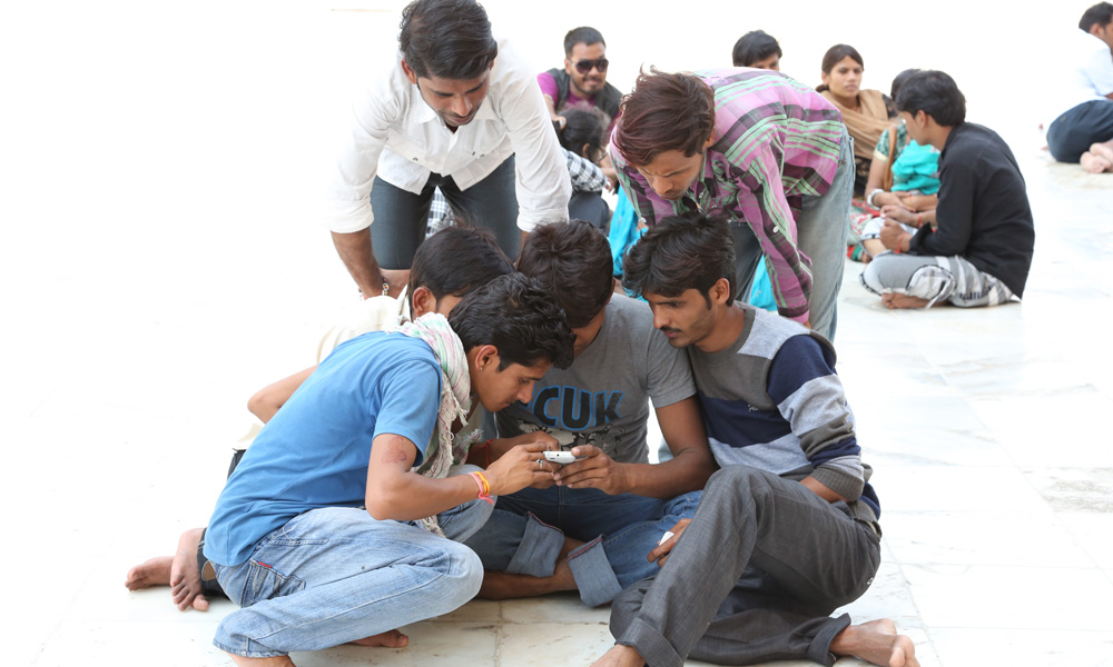 Photo of a group gathering around a man with his mobile phone